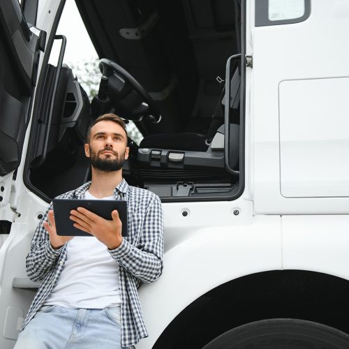 Young handsome truck driver is standing with a tablet near the truck.